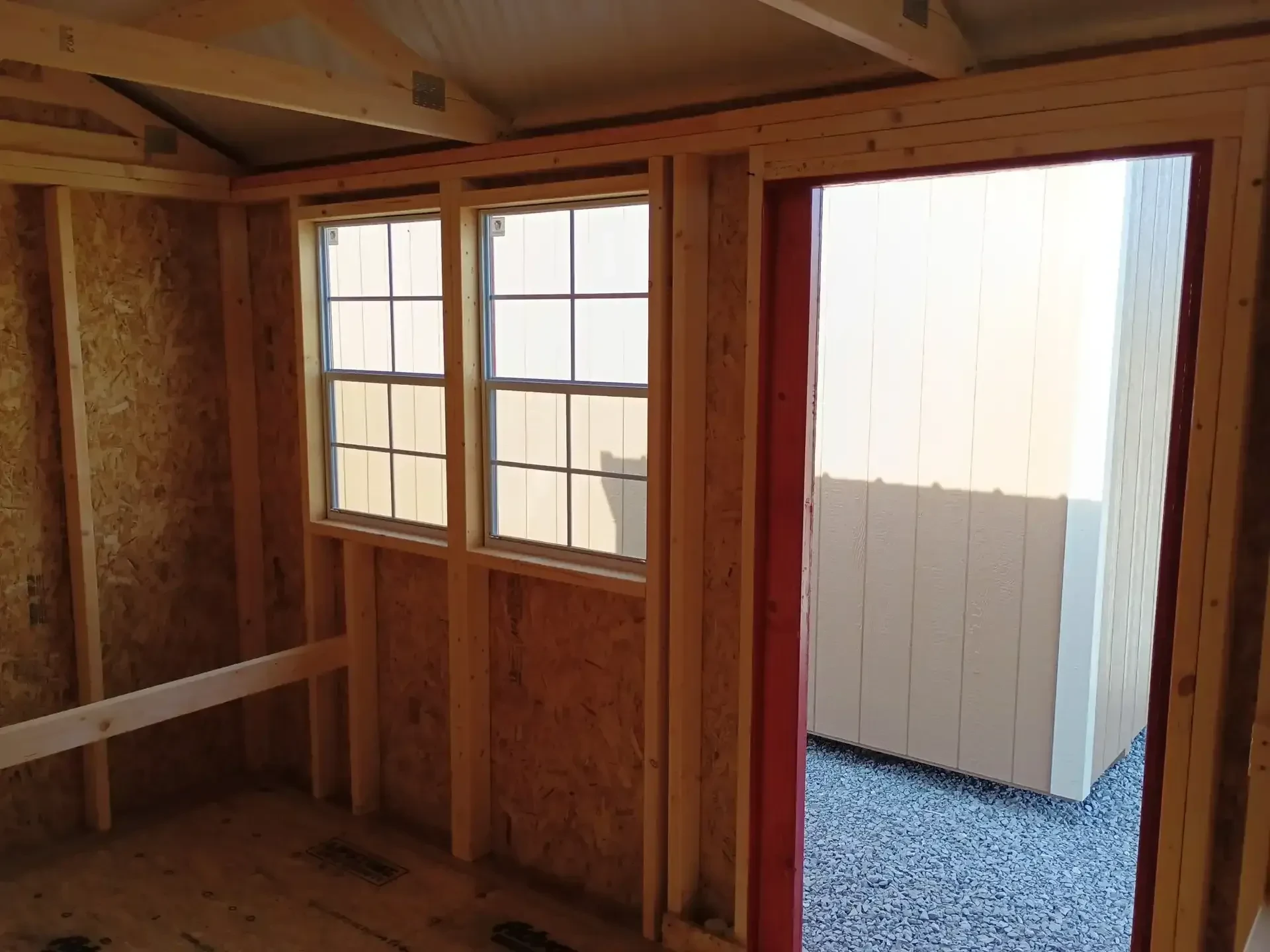 looking out of a chicken coop with the barn door open and two windows on the wall next to each other