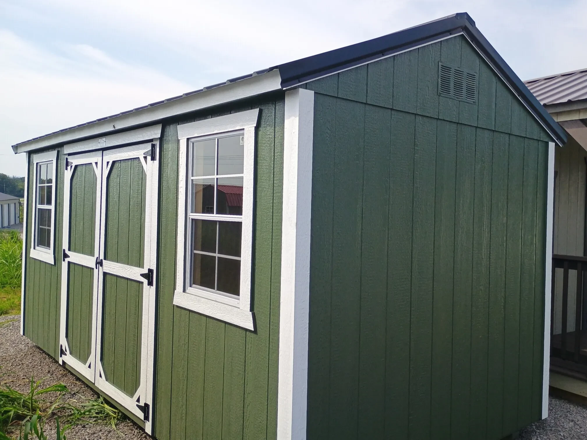 a green garden shed with white trim, double doors, and two windows