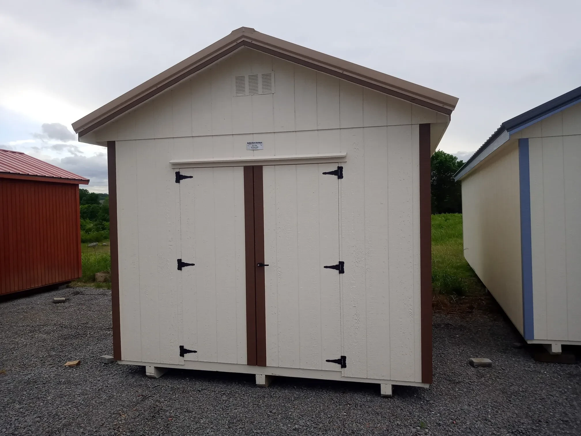 a white wood shed with a roof overhang and double doors