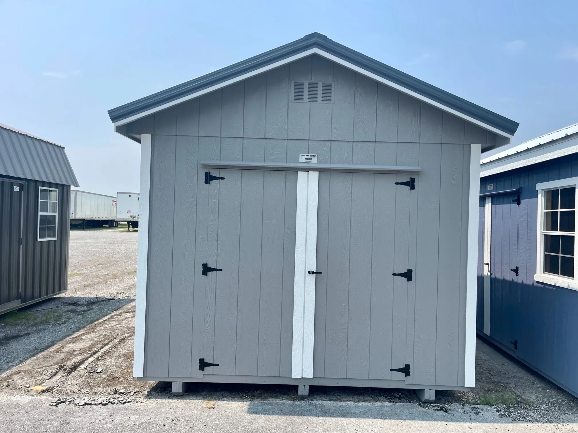 a light gray utility shed with a roof overhang and double doors