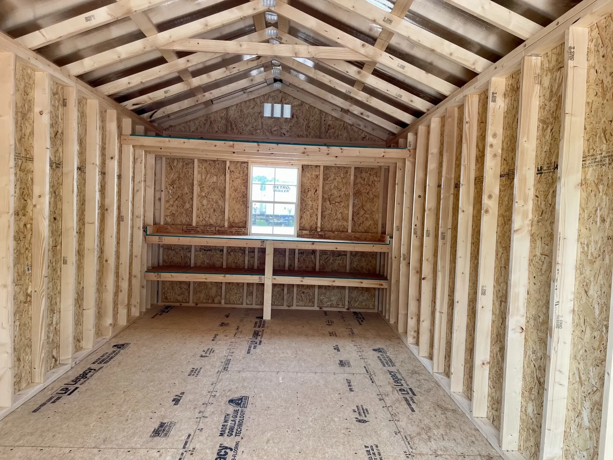 inside a wood utility shed with double shelves, a loft, and a window along the back wall