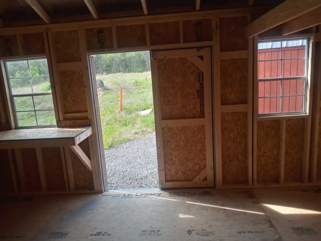 inside a wood garden shed with a workbench and the double doors open