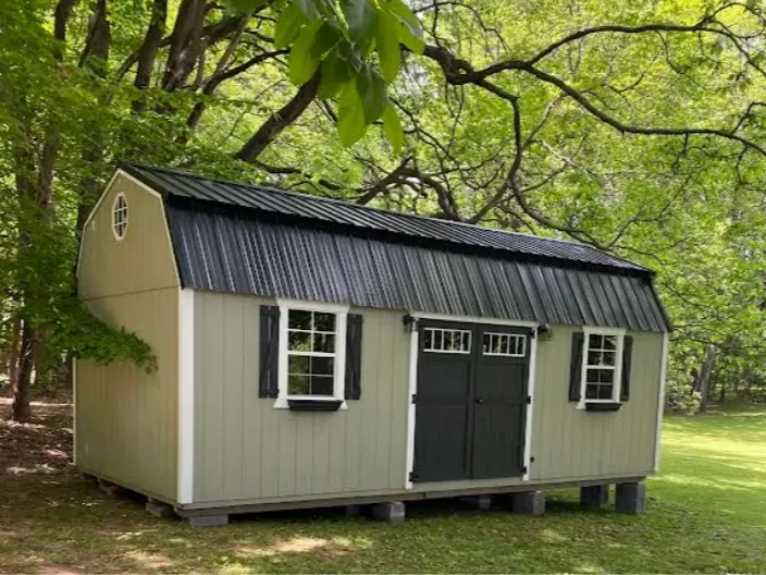 a light green side lofted shed with painted double doors with windows in them and other windows with shutters