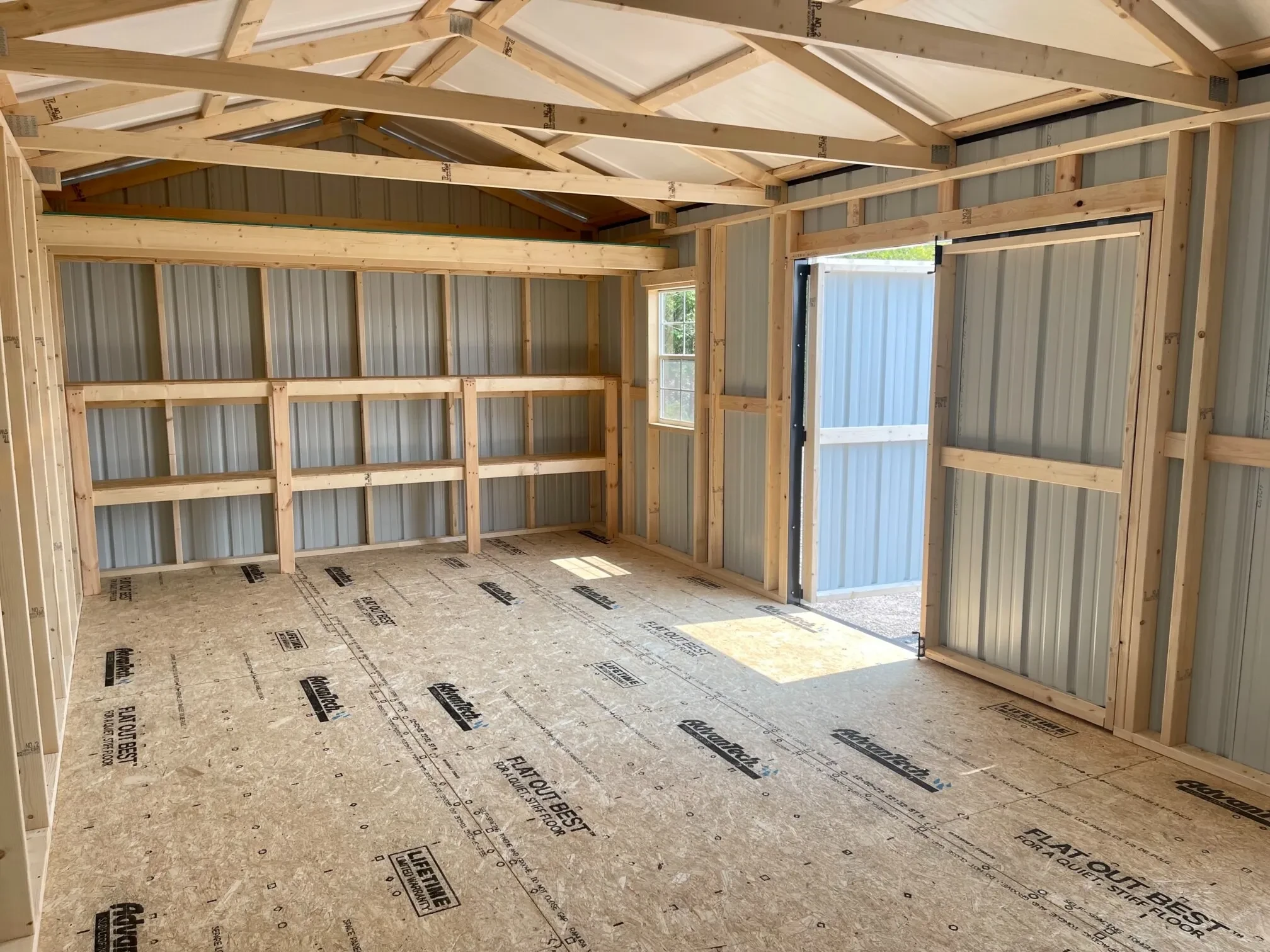 the inside of a metal garage shed with double shelves, a loft, and the double doors open next to a window