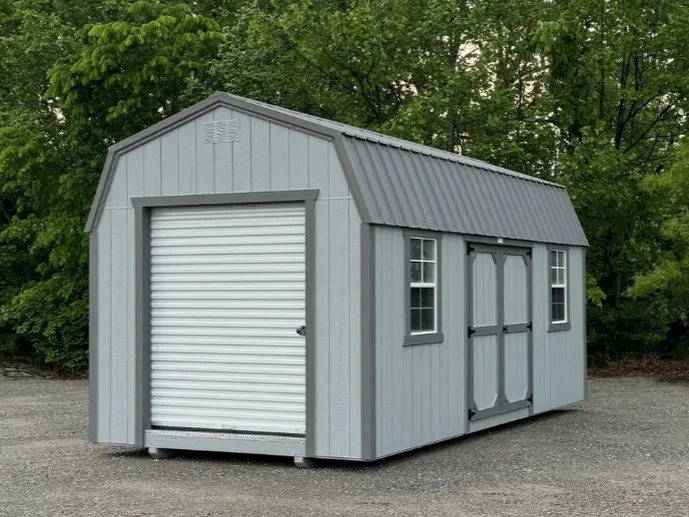 a gray lofted garage with a rollup garage door in the end and double doors and two windows in the side