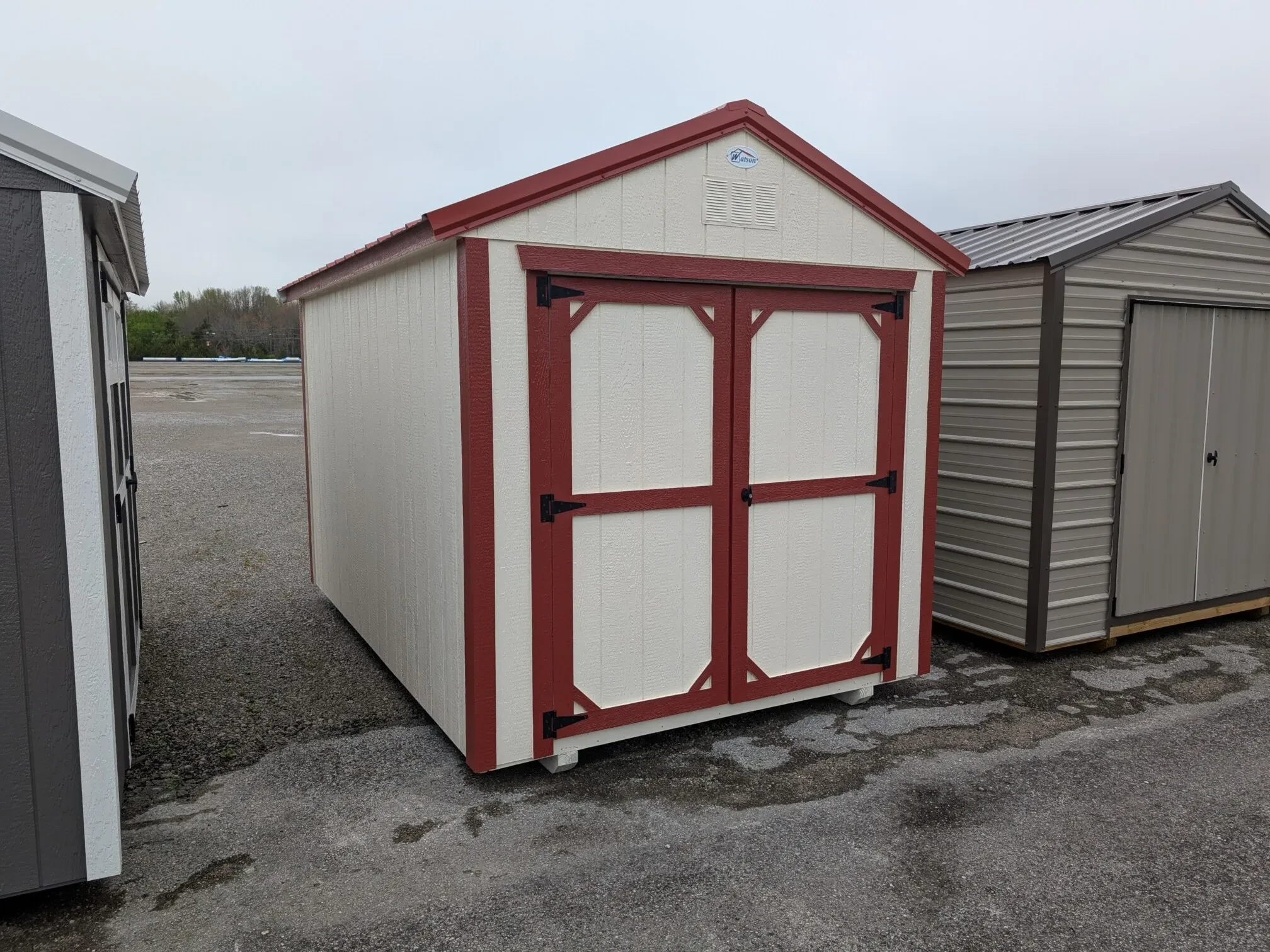a white wood utility shed with double doors and red trim
