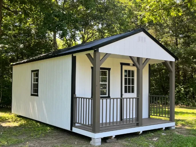 a white cabin with black roof and trim and a 4' porch on the front