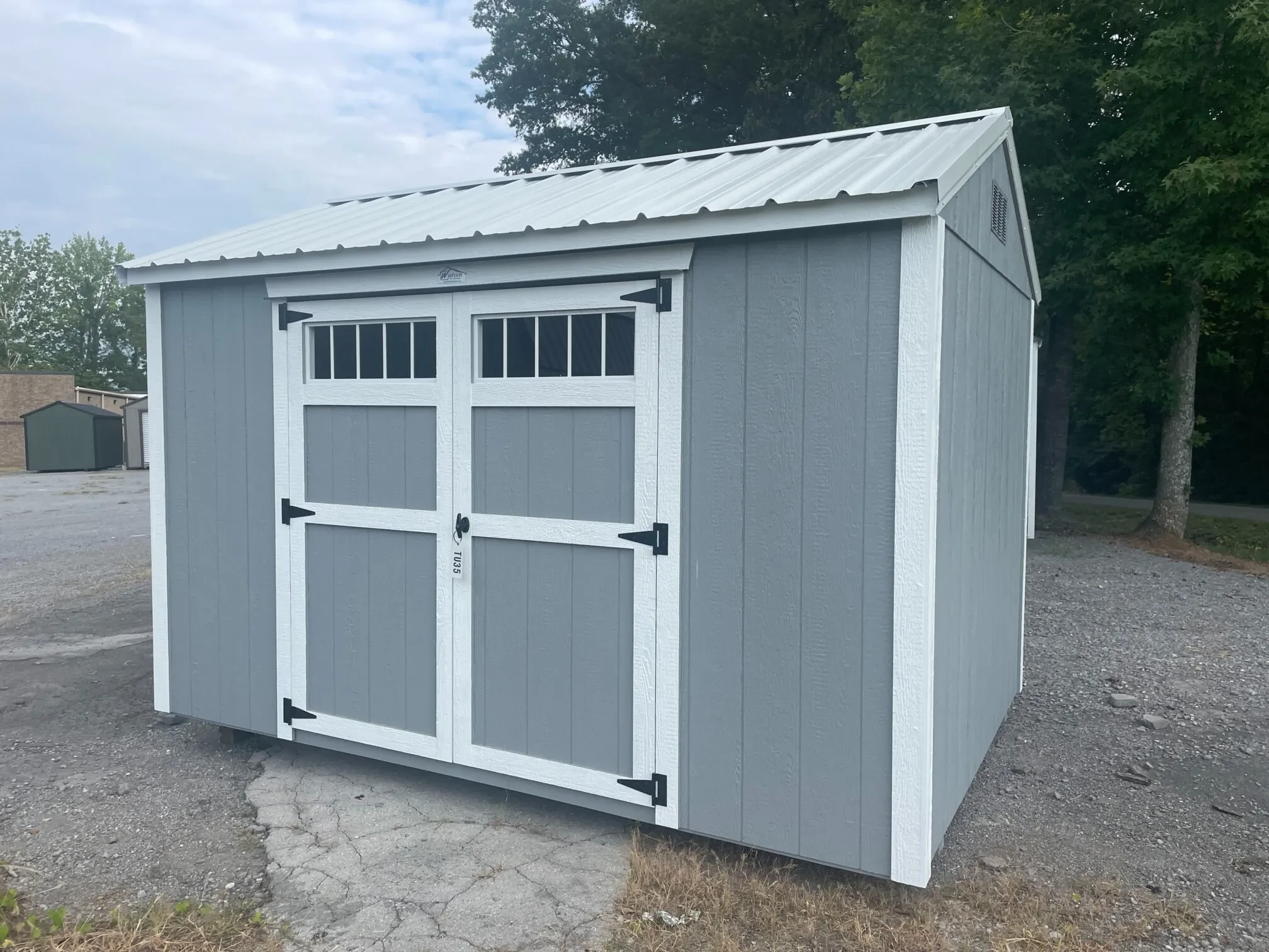 a light gray colored wood shed with double doors that have transom windows at the top of them