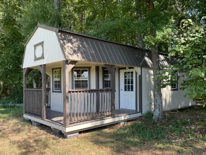 a white deluxe lofted cabin with a L shaped porch that is nestled in among trees