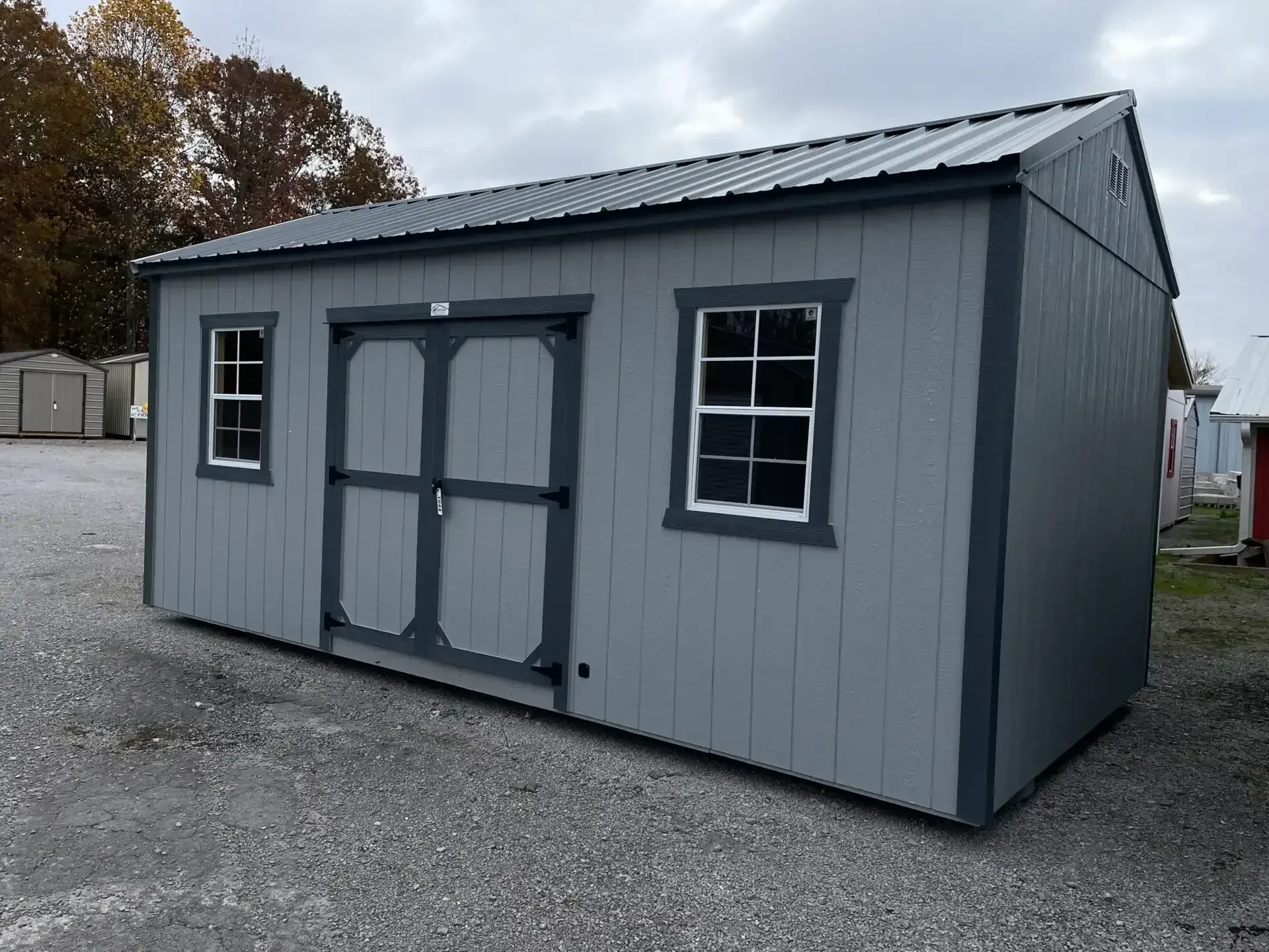 a light gray wood garden shed with double doors and two windows