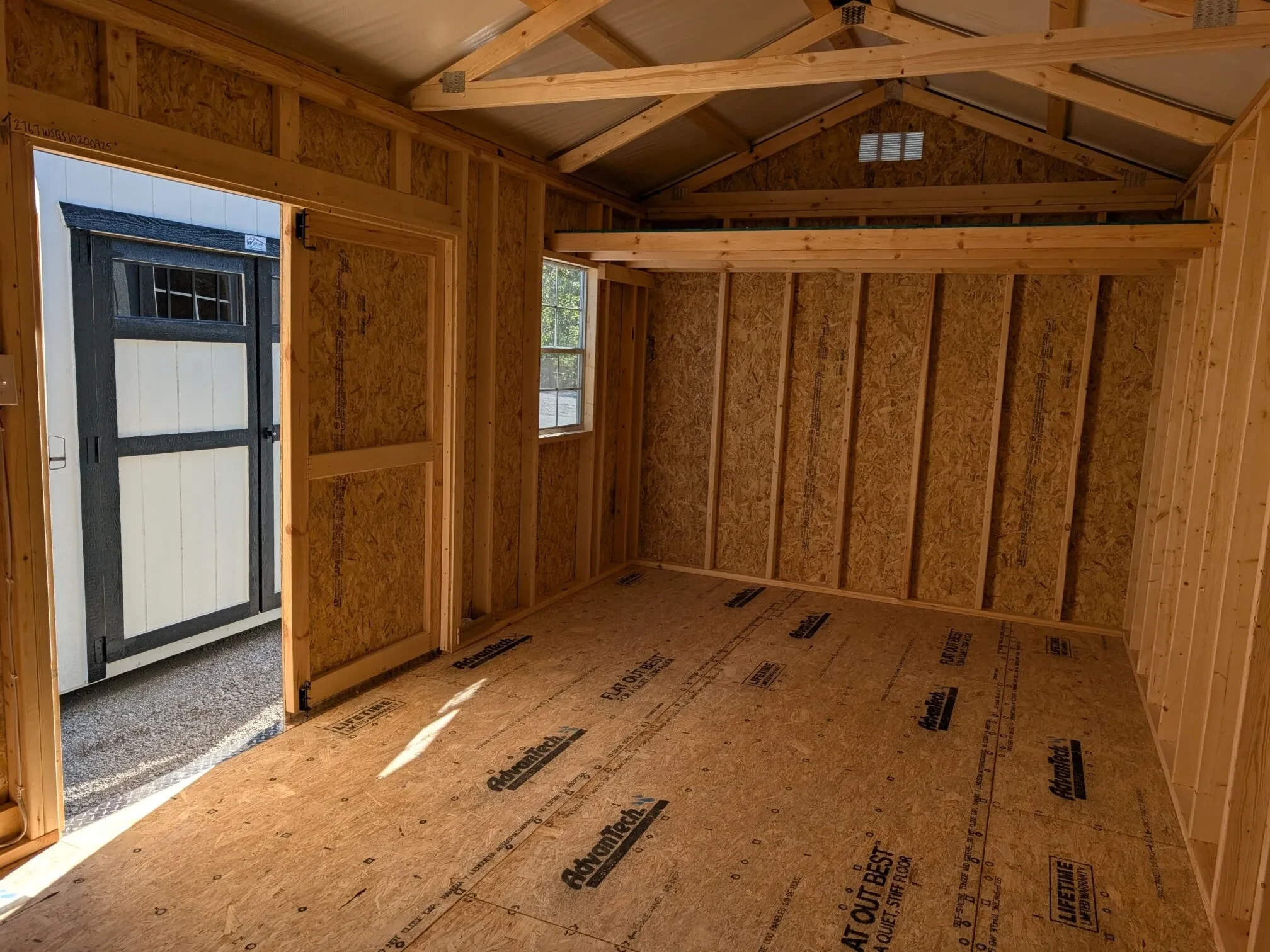 inside view of a wood shed with a loft on the left side and a window and one of the double doors open