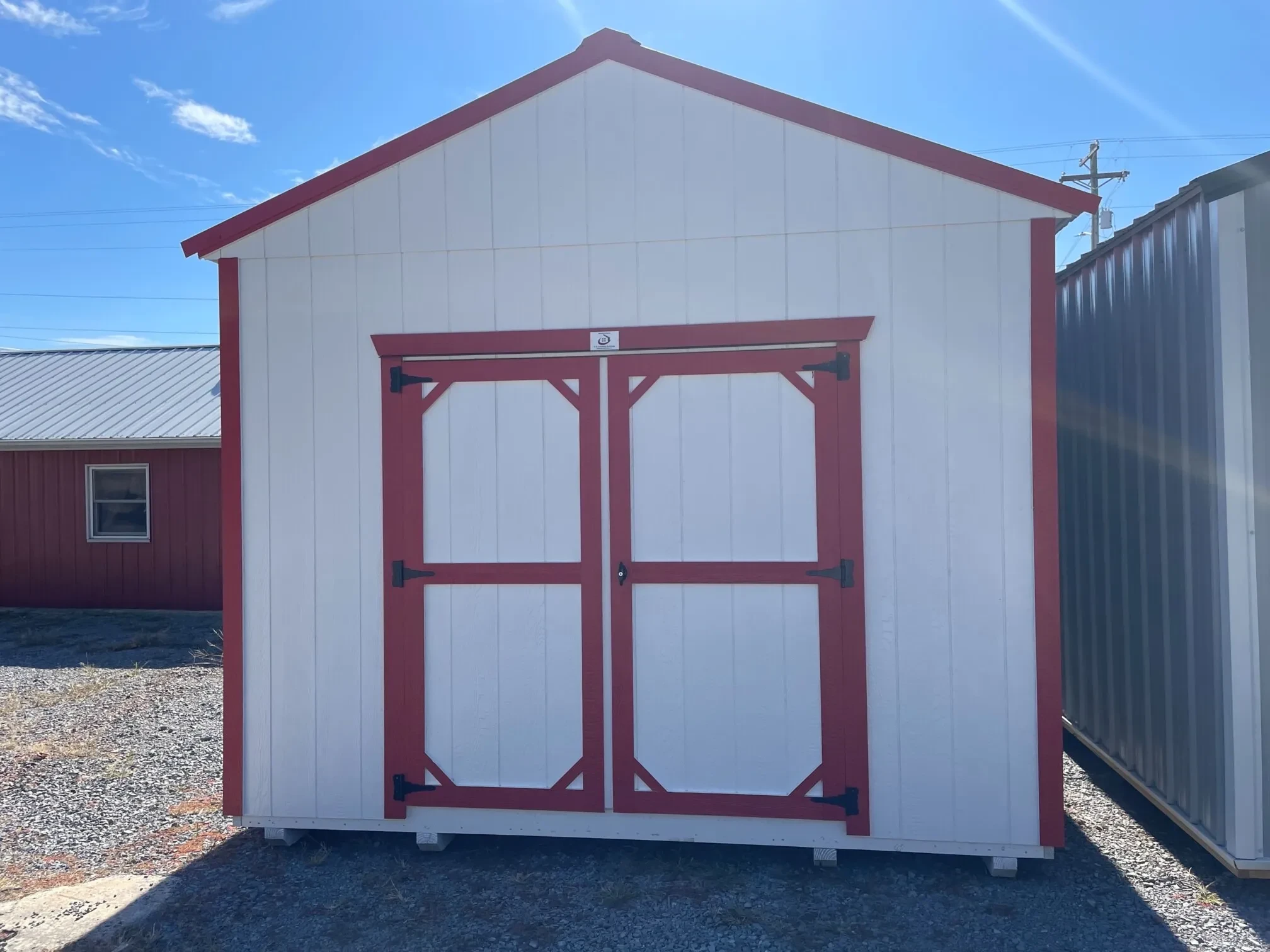 a white wood utility shed with red trim and double doors