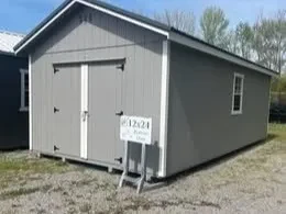 a large gray shed with a roof overhand and double doors and a 2x3 window