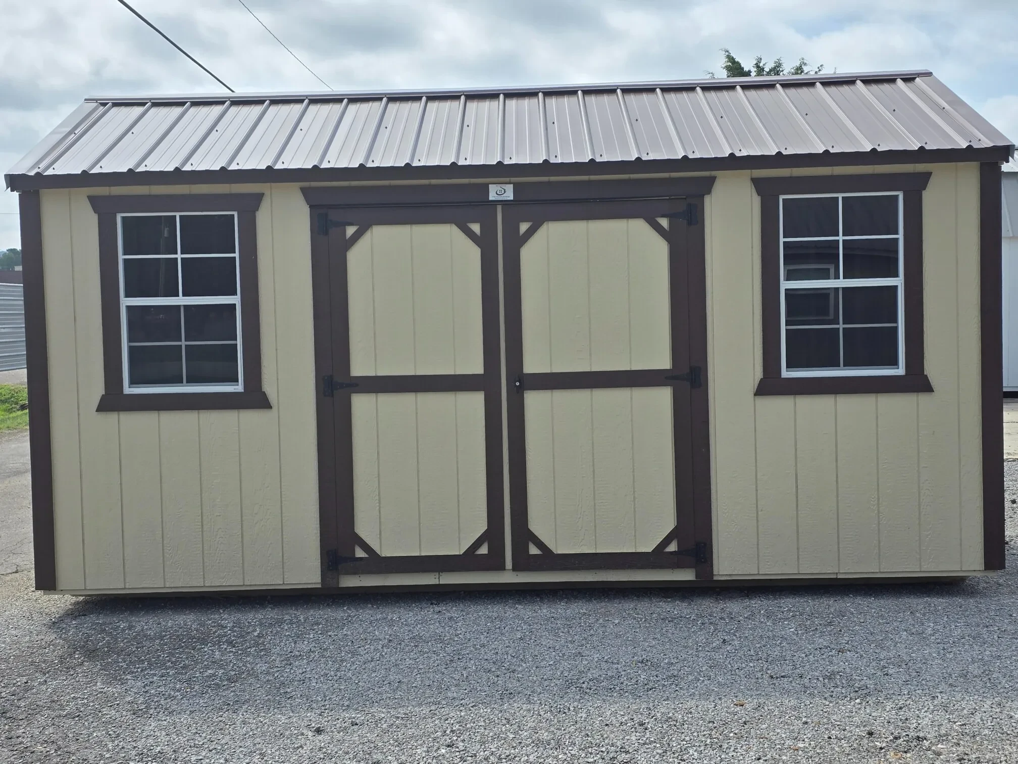 a beige colored garden shed with double doors and a window on each side of the doors