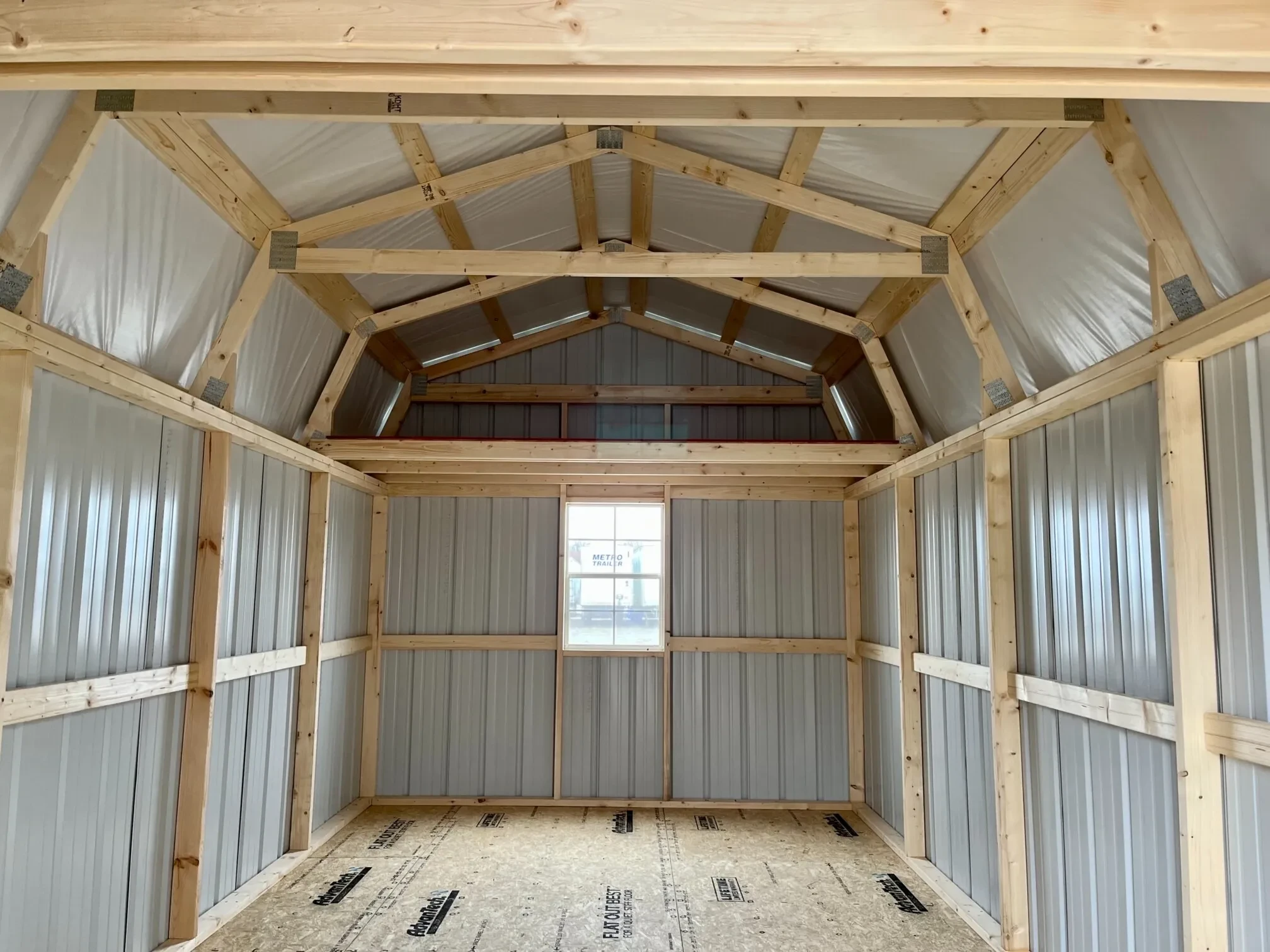 inside a metal lofted barn looking at the back wall which has a 2x3 window and a4' loft above it