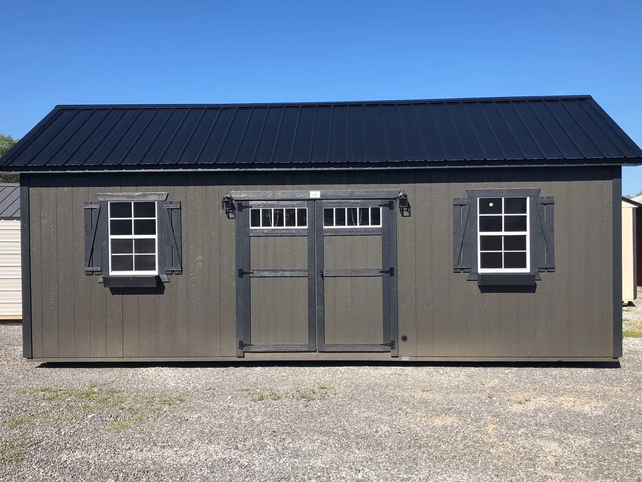 a brown garden with a roof overhang, double doors with transom windows, and two windows with shutters
