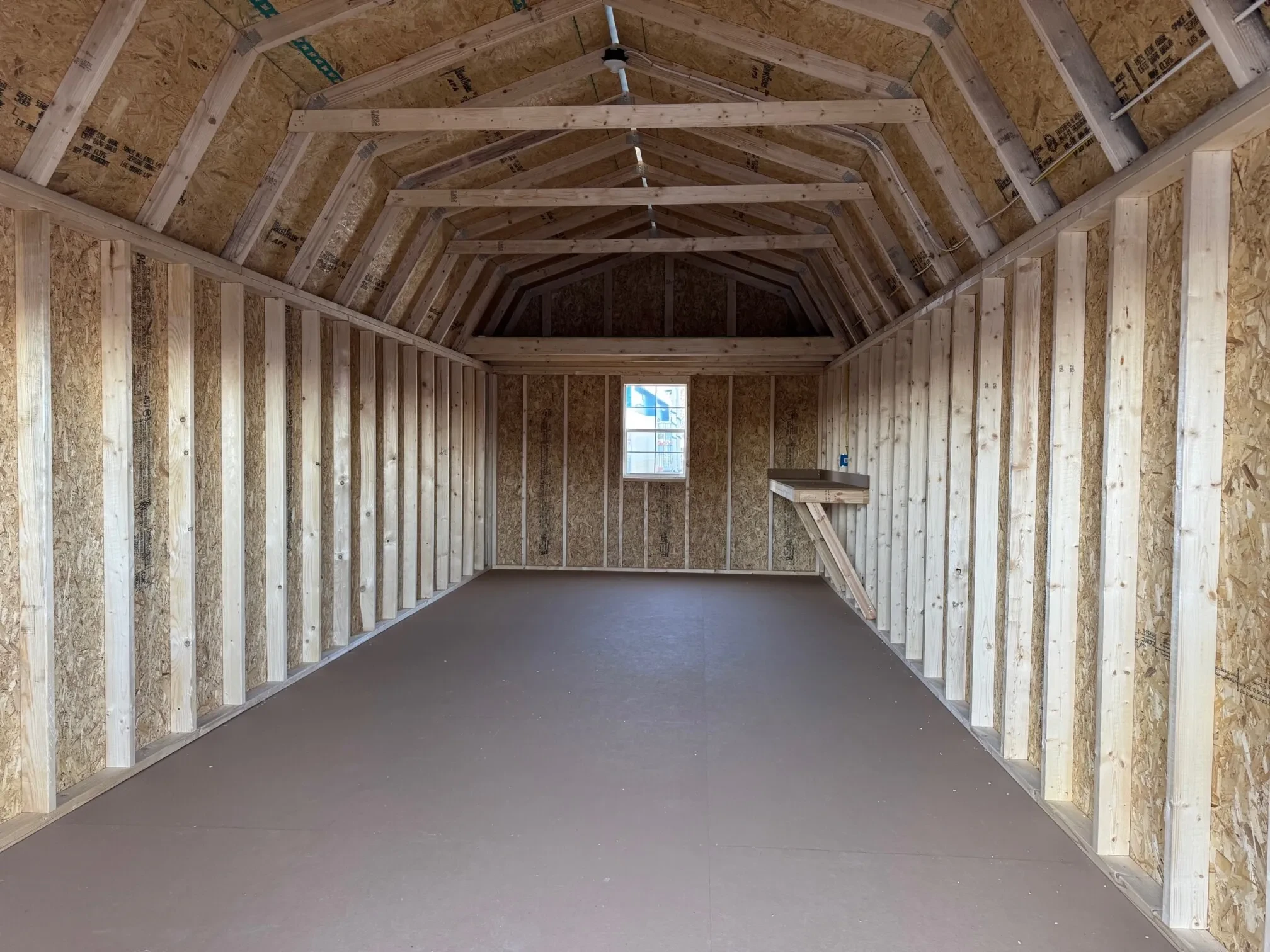 inside a large lofted barn with a loft above a 2x3 window on the back wall and a workbench on the right wall