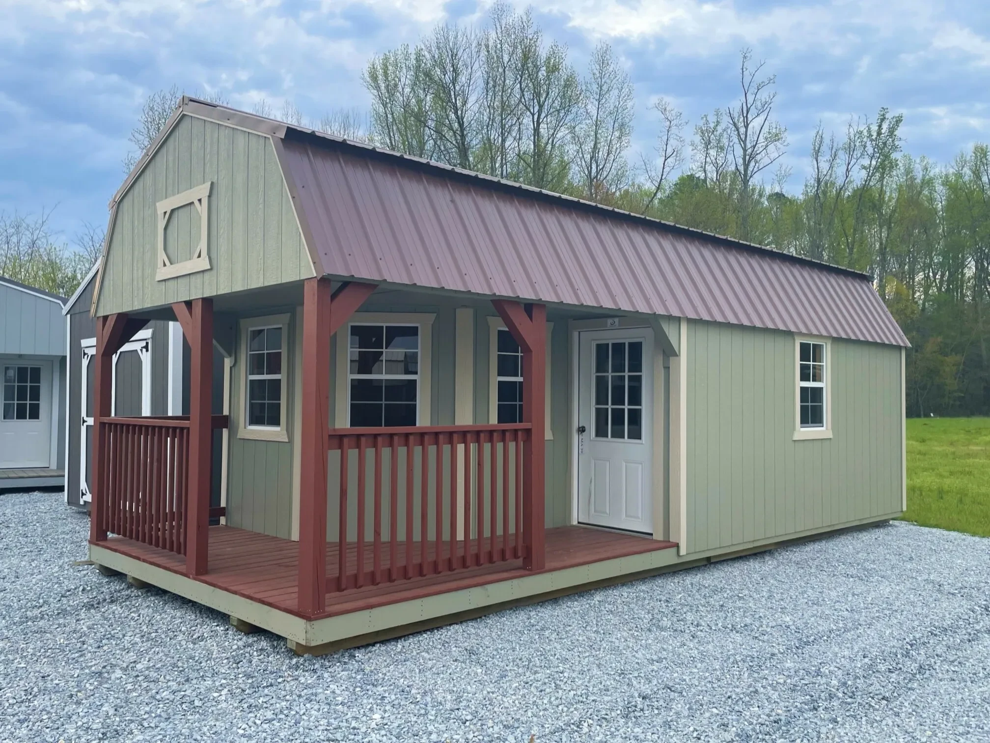 a light green shed with a L shaped stained wood porch with a walk-in door and many windows
