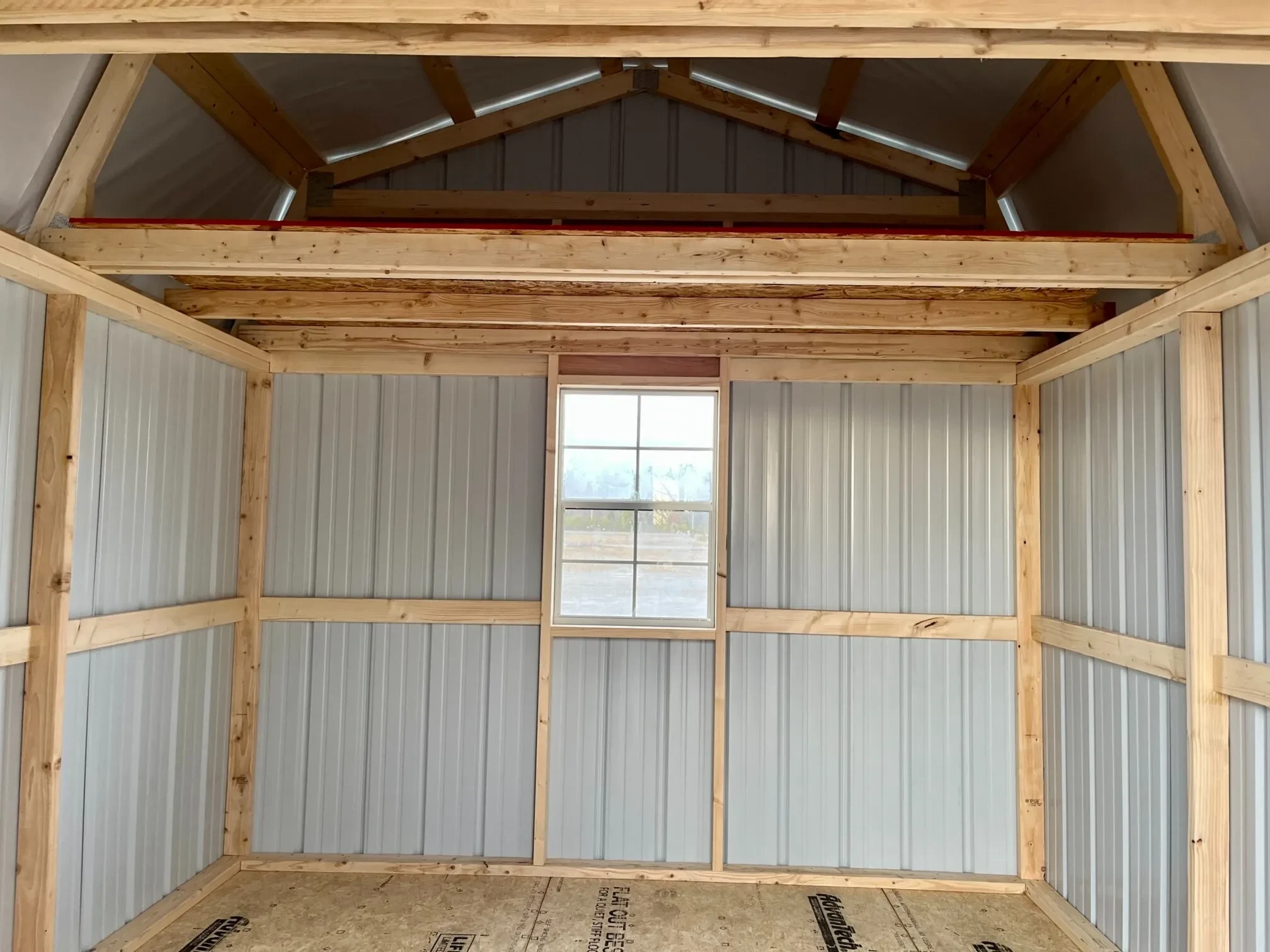 a window on the back wall underneath a 4' loft, inside of a metal lofted barn