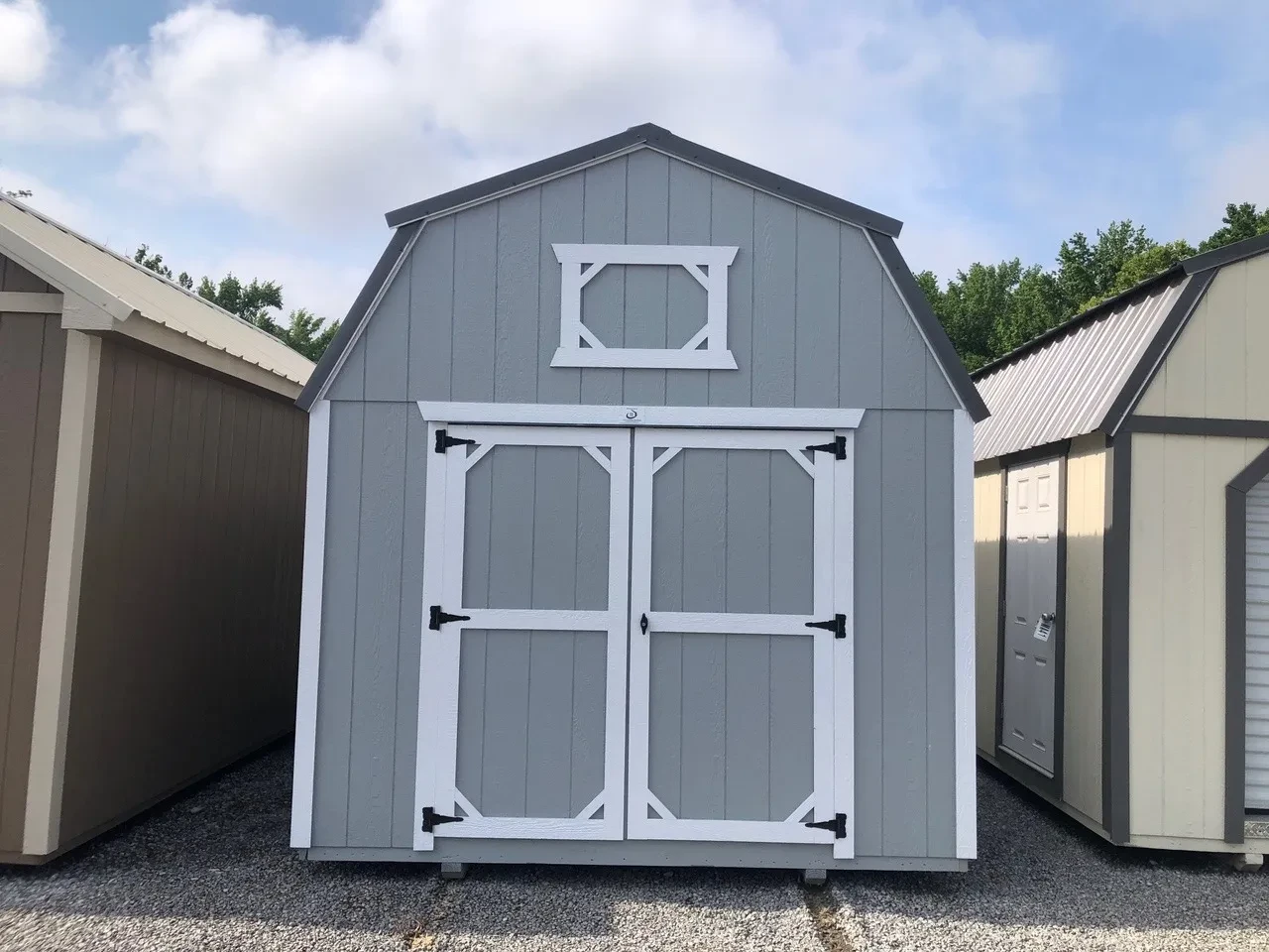 a lofted barn painted gray with white trim. It has double doors and decorative loft trim above the doors