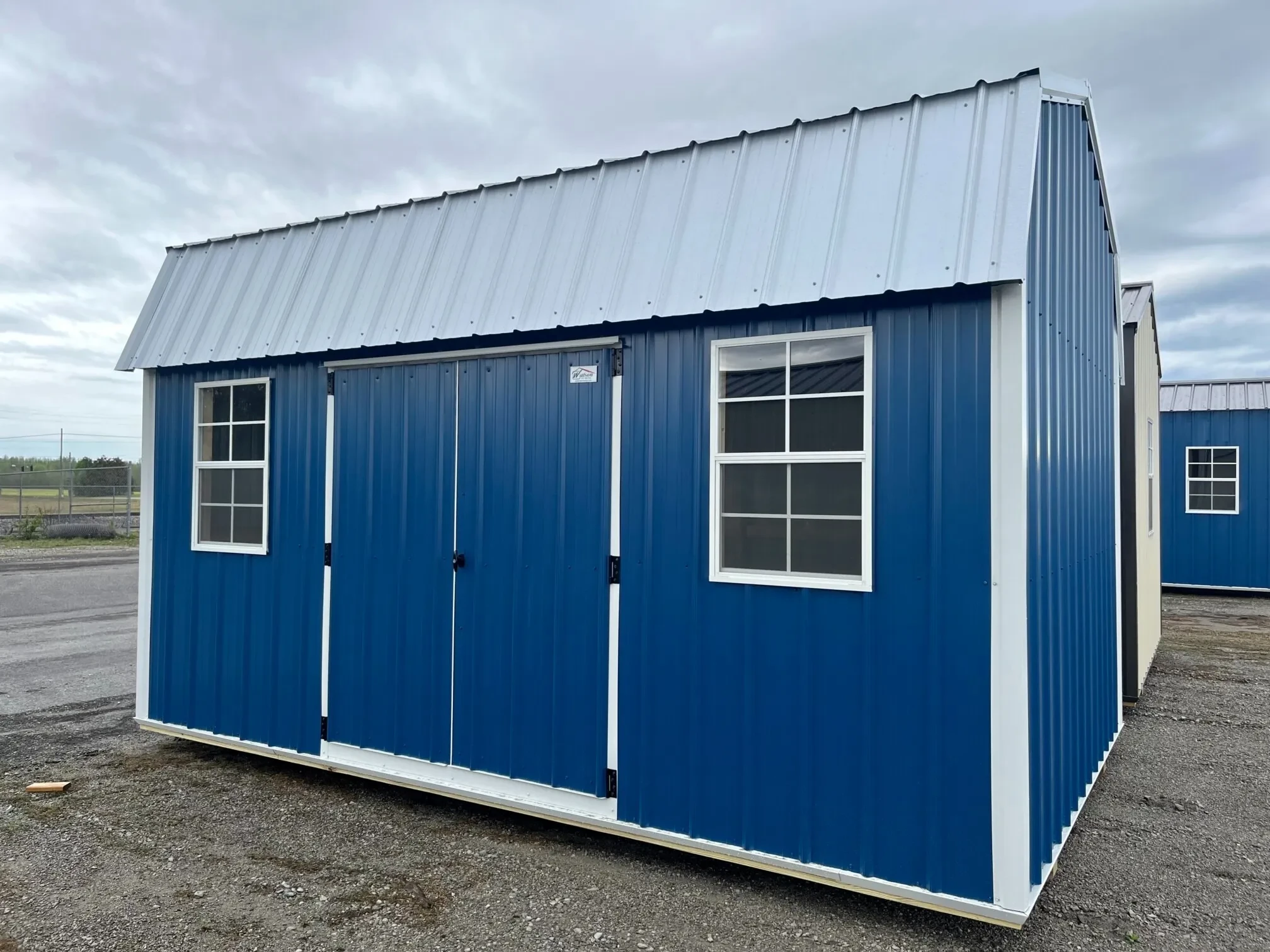 a blue side lofted barn with a galvalume roof and white trim and two windows