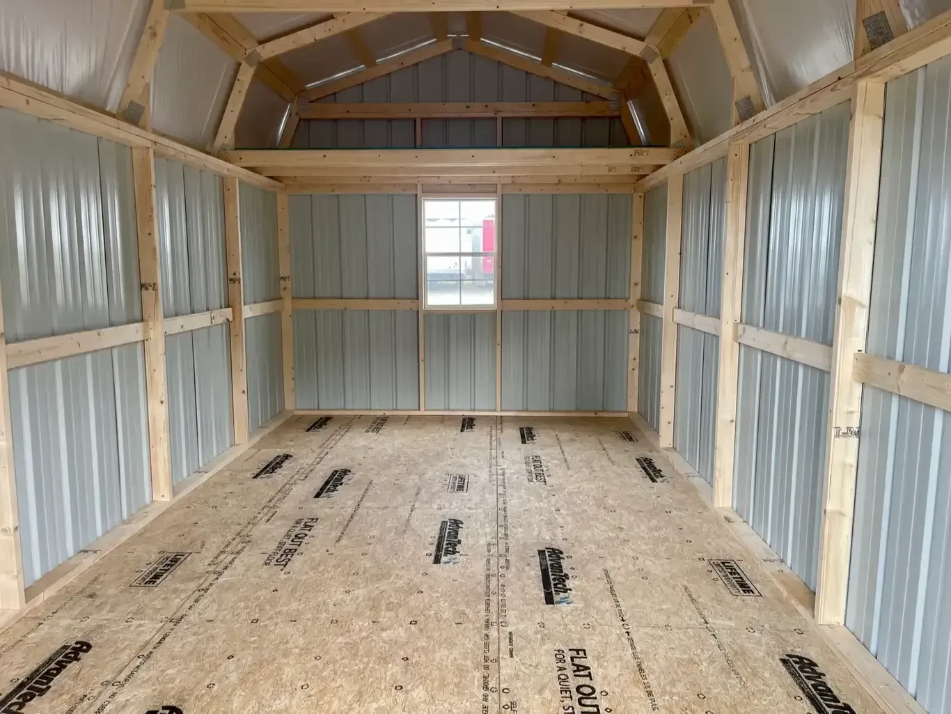 a window in the middle of the back wall under a loft inside a metal lofted barn