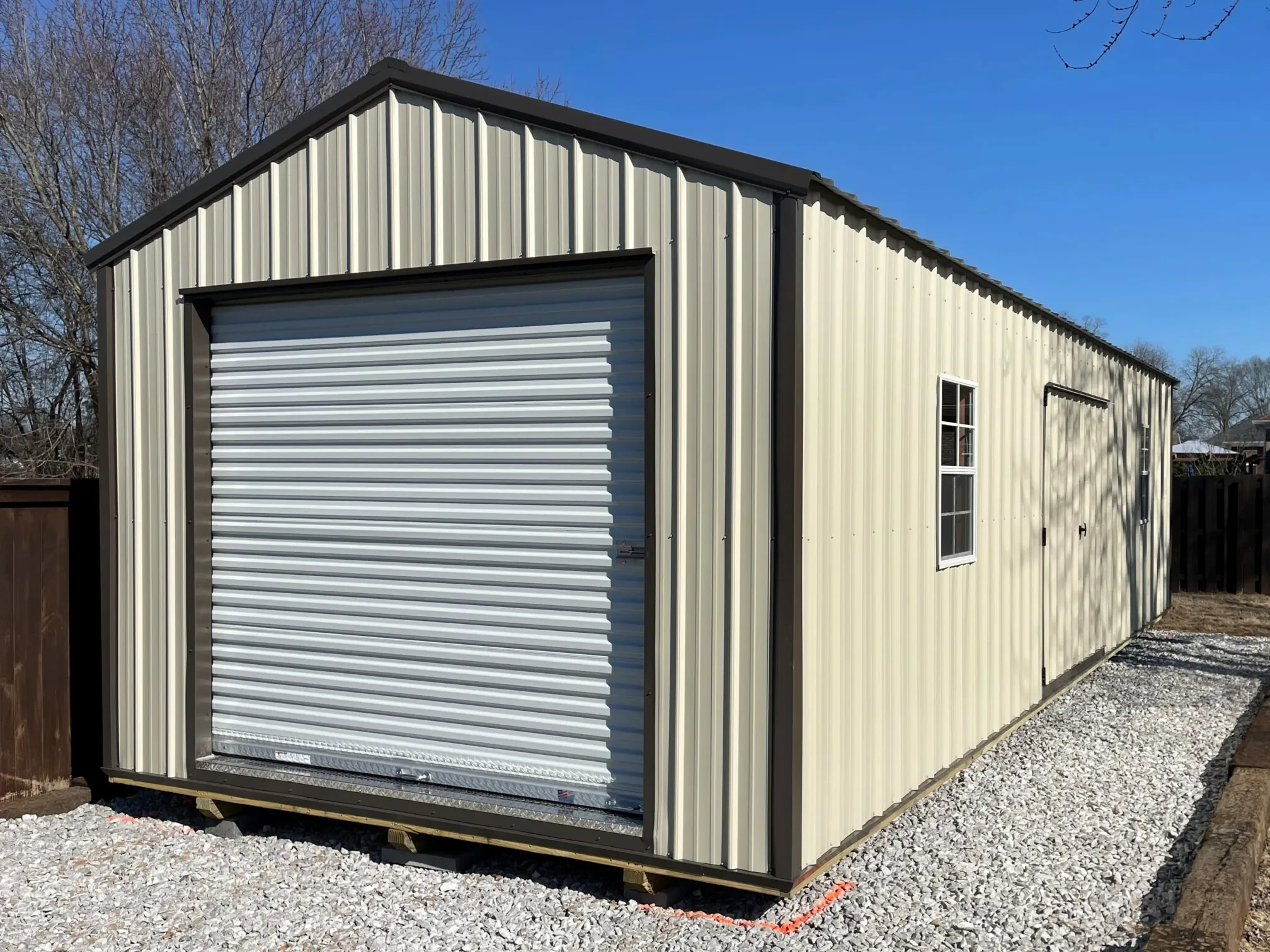 a long metal garage shed with a garage door in the end and double doors and two windows in the side