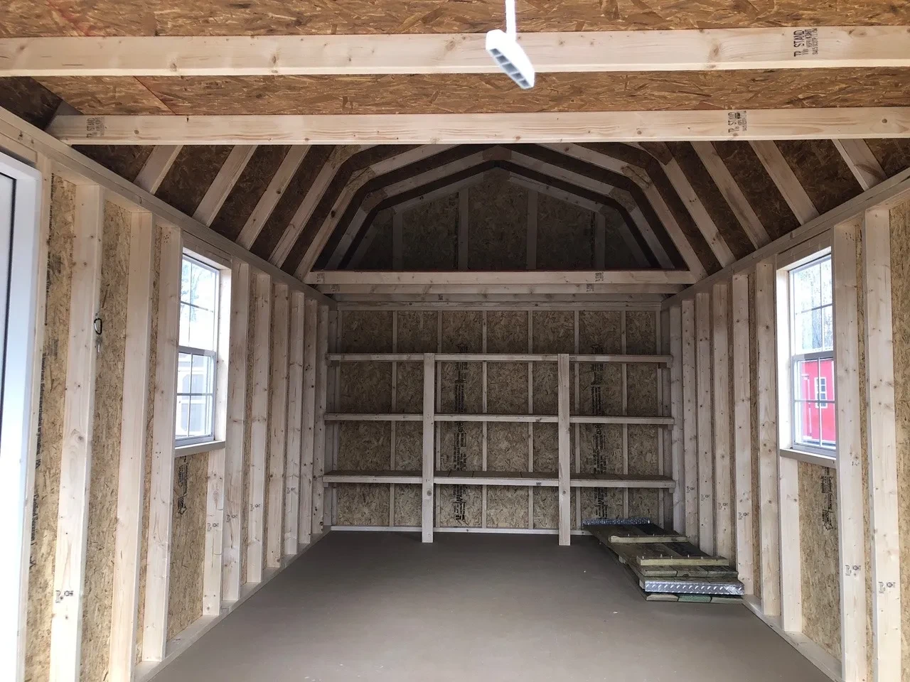 inside a lofted garage showing a loft above 3-tier shelving on the back wall and a window on the left and right walls