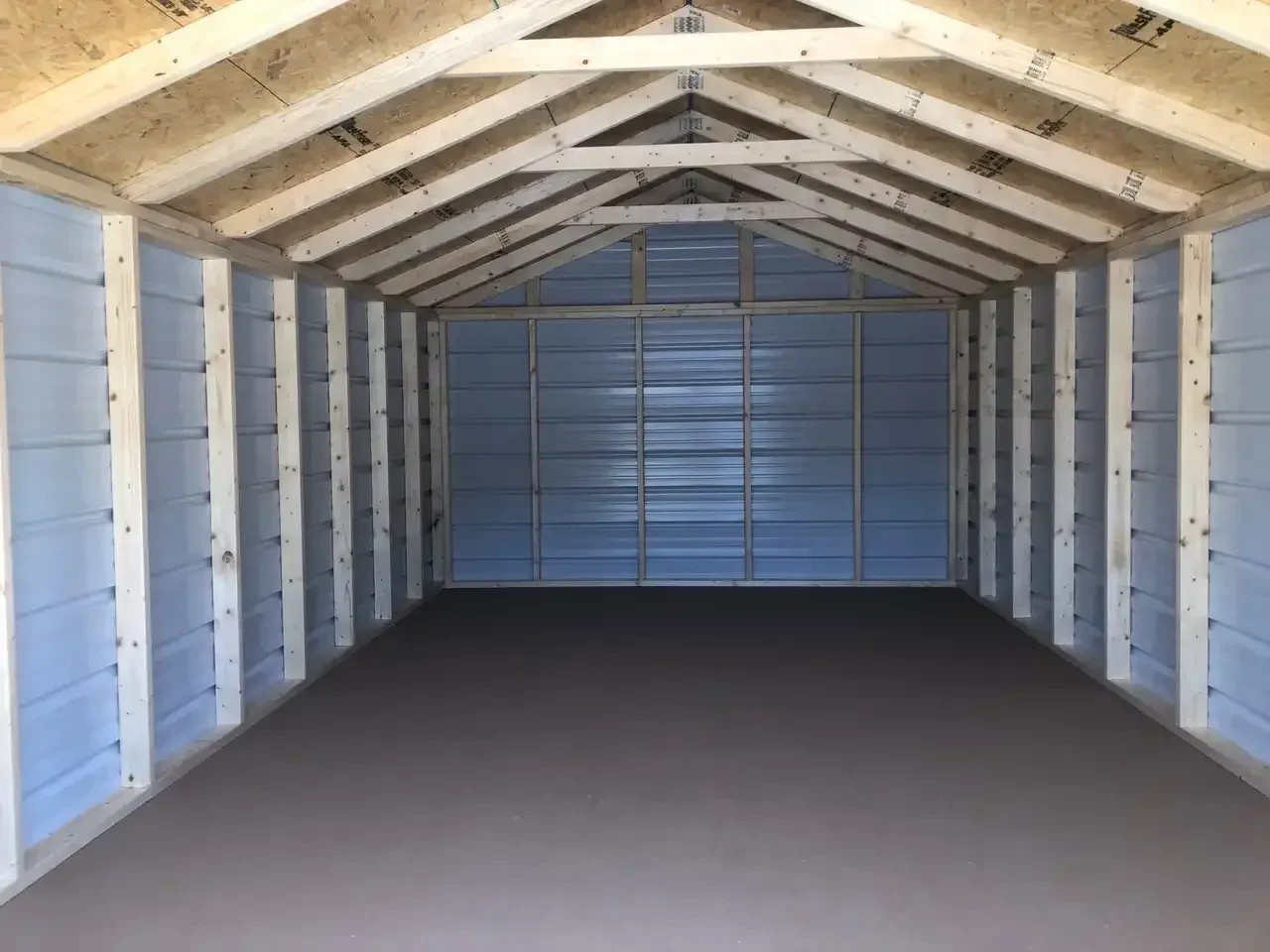 inside a wide metal utility shed that shows the trusses and a solid floor inside