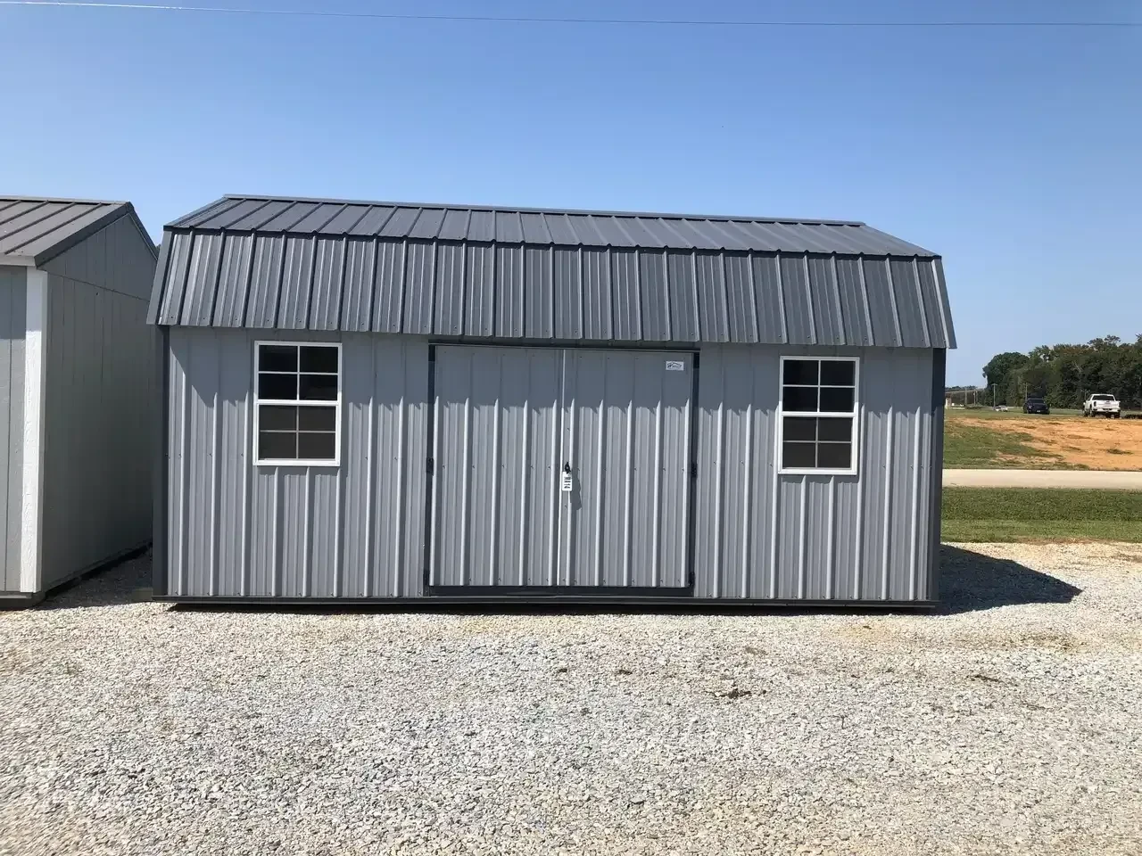 a gray metal side lofted barn with double doors and two windows