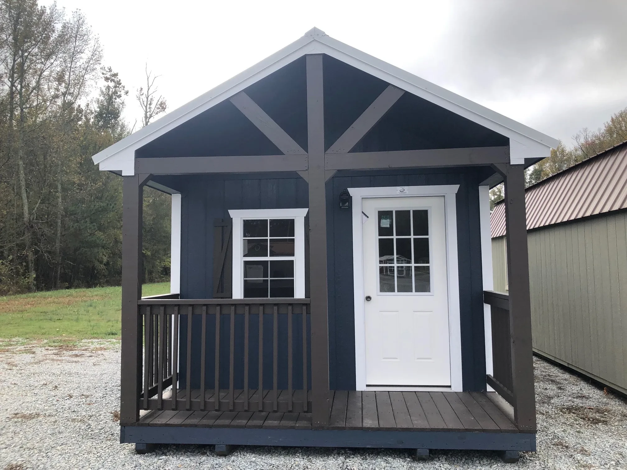 the front of a blue cabin with a brown porch, a white 9-lite walk-in door, and a window