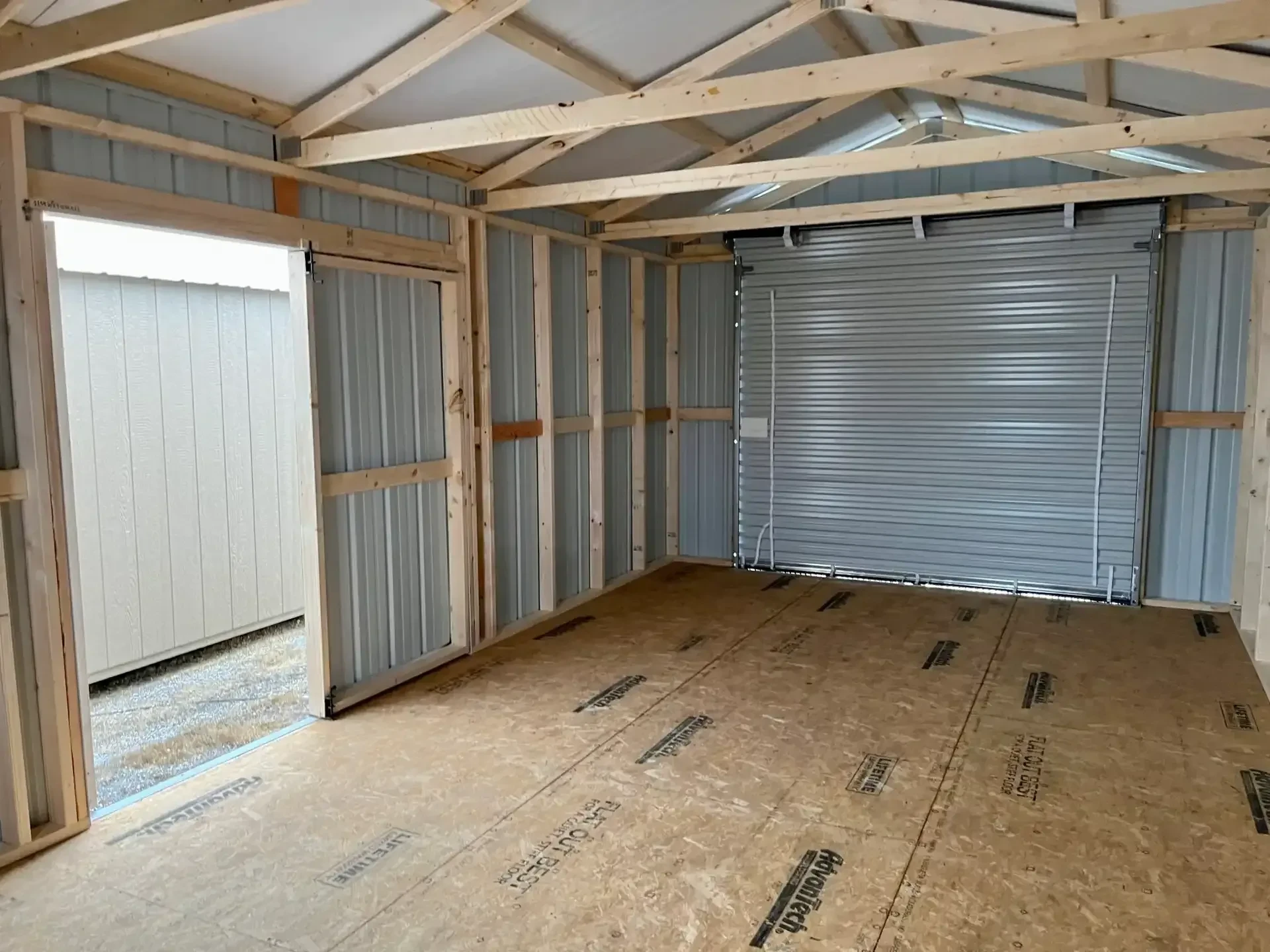 inside a metal garage looking at the 8x7 rollup door that is closed and the double doors on the side which are open