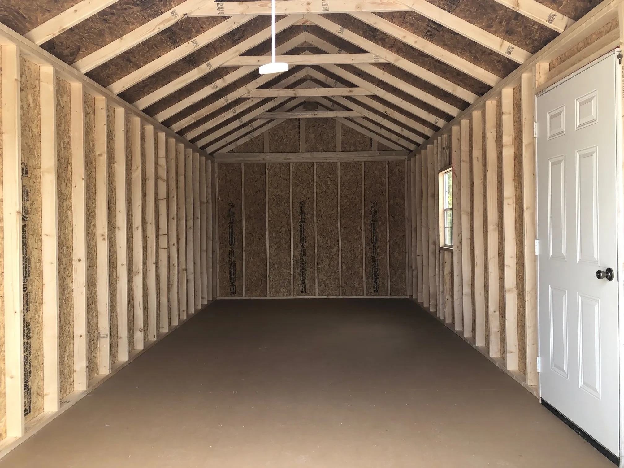 inside a wood garage showing a solid floor and a window and walk-in door in the right wall