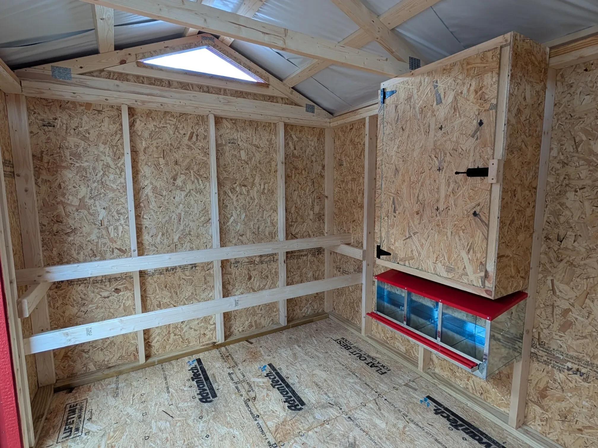 inside a red chicken coop with two roosting bars, three nesting boxes and a storage cabinet above the nesting boxes