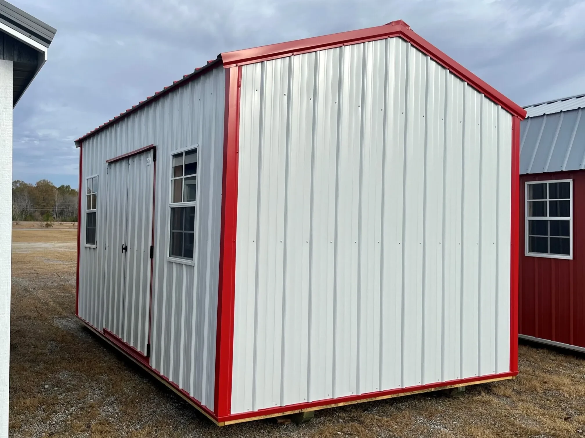 a white metal garden shed with two windows and red trim