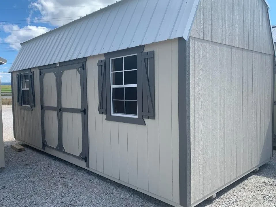 a large stone colored side lofted barn with two windows with shutters and double doors