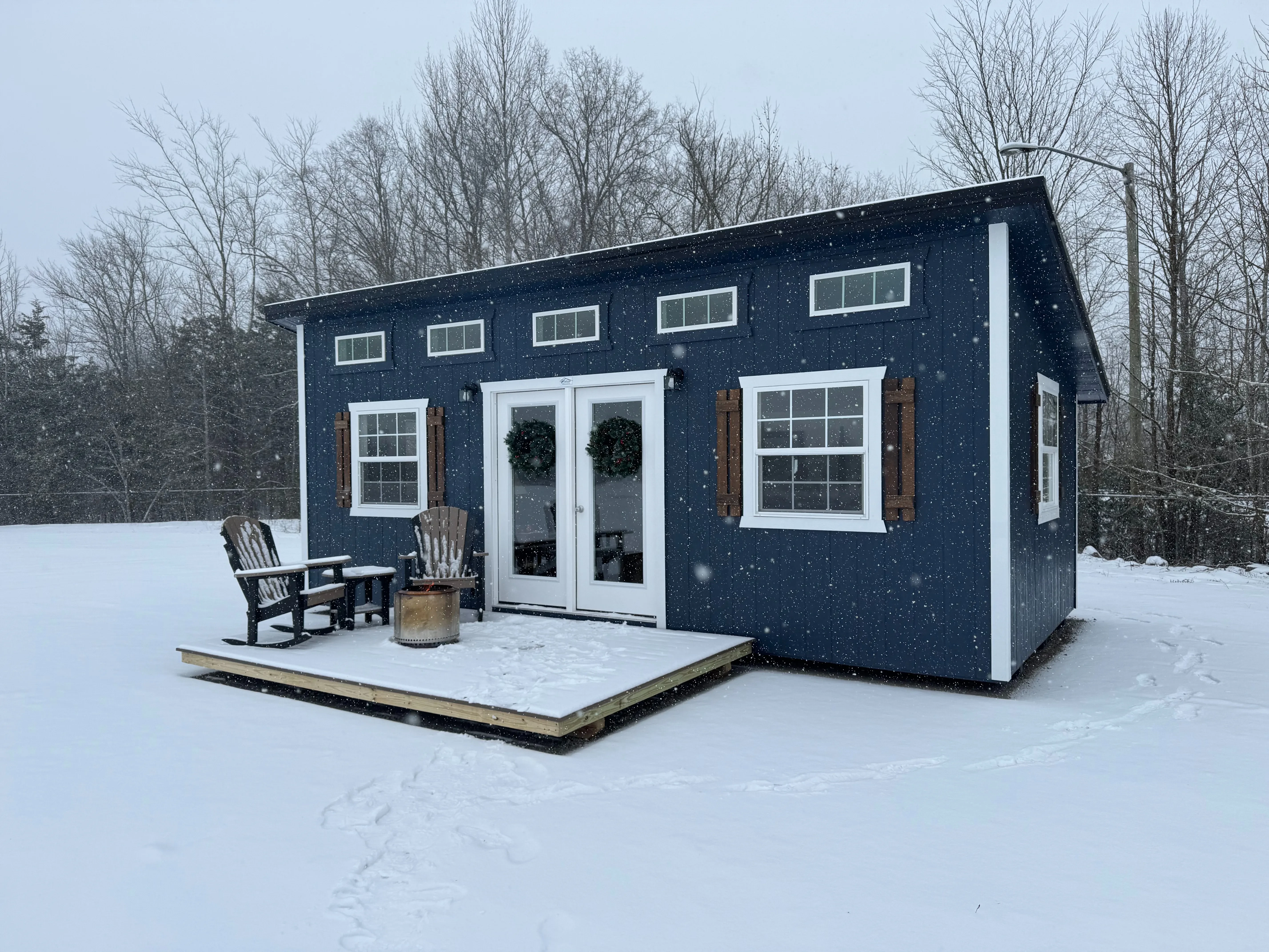 a dark blue studio shed in the snow with many windows and glass patio doors and a porch on the front