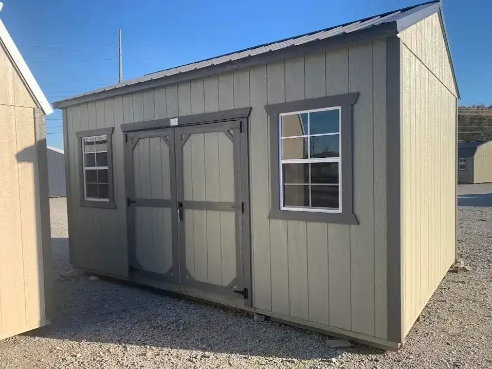 a large clay colored garden shed with double doors and a 2x3 window on each side of them