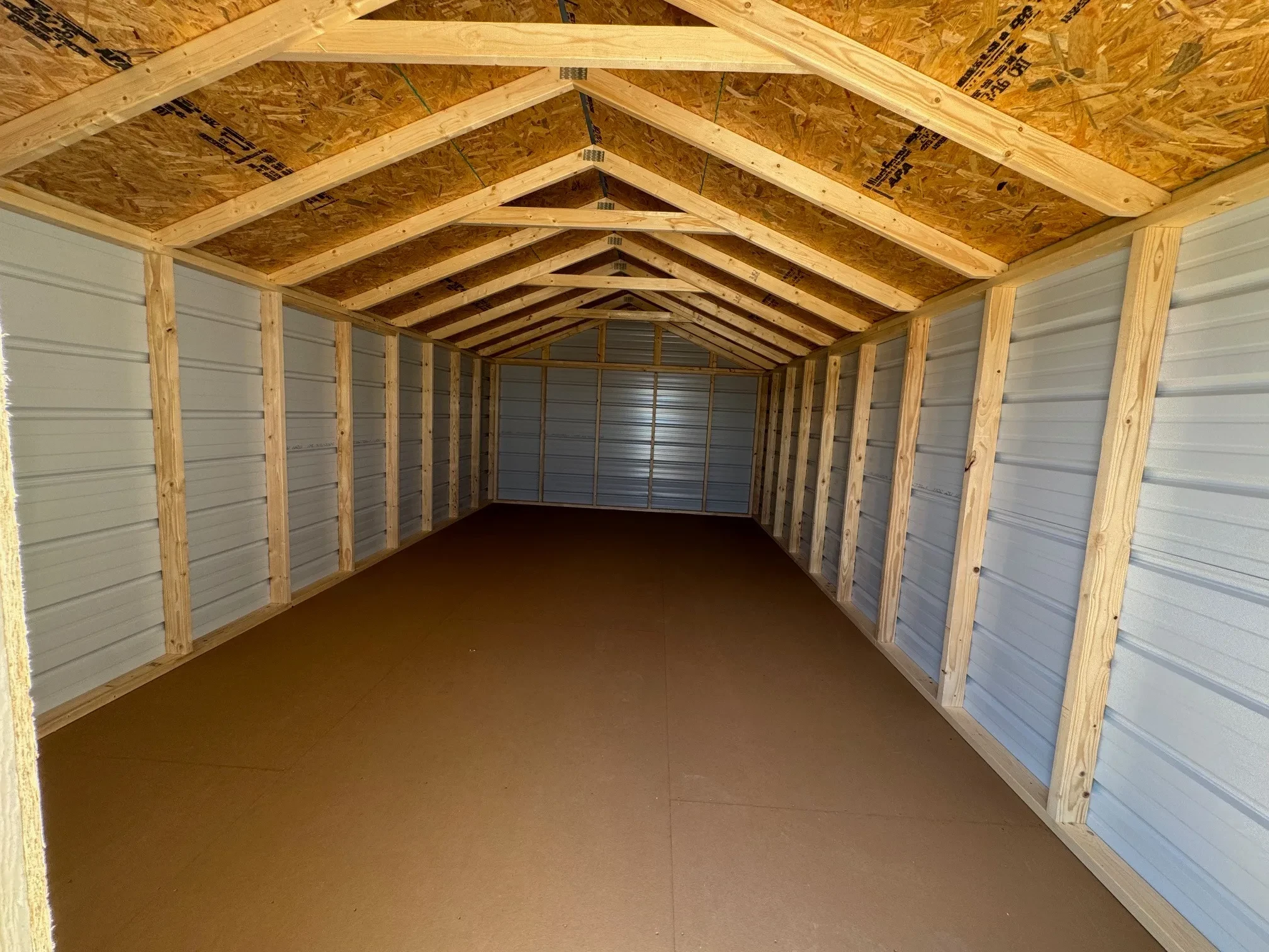 inside a long metal utility shed with lumber framing and a solid floor