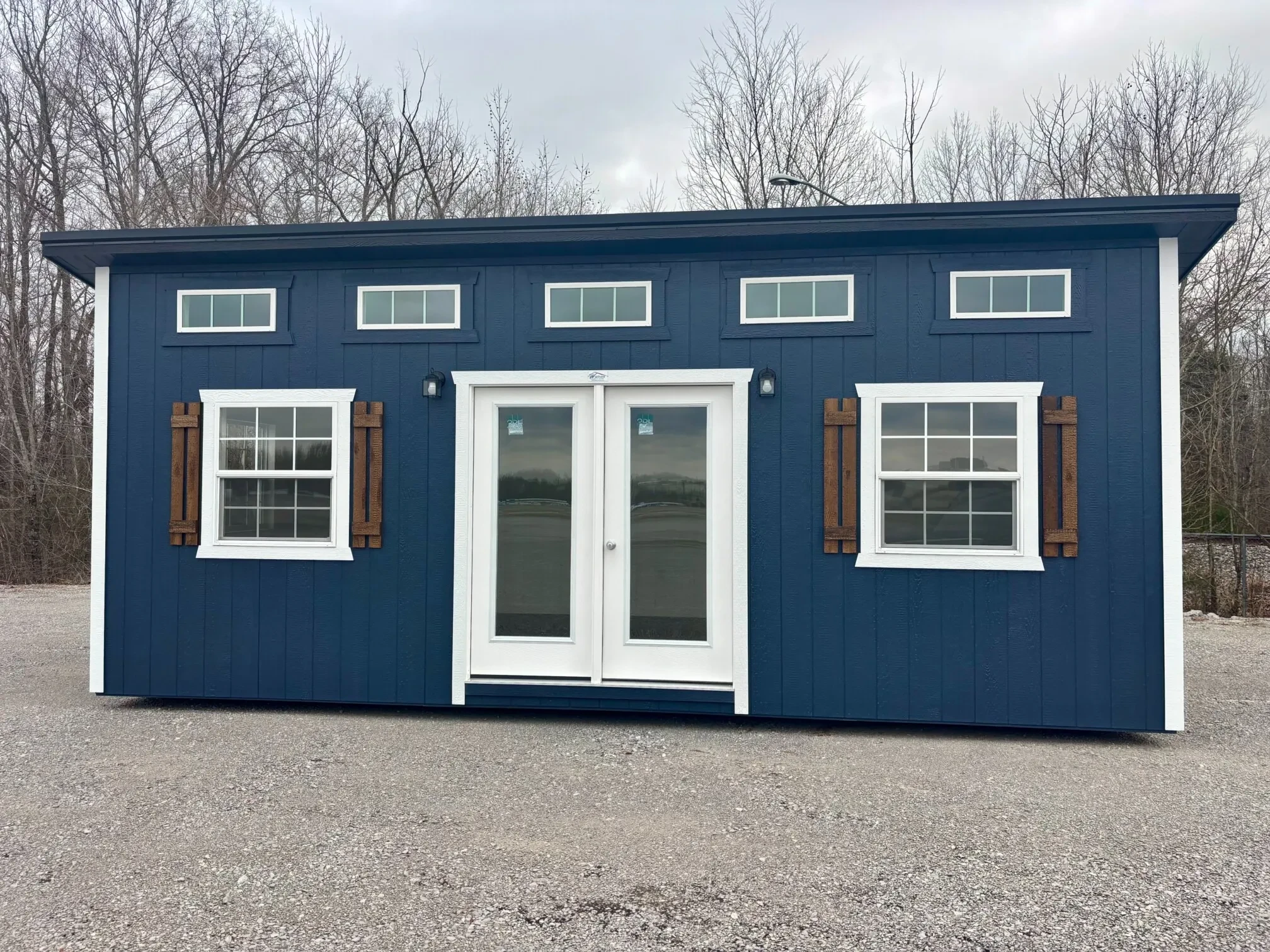 a blue studio shed with french doors in the front, vinyl insulated windows, and five transom windows up towards the roof