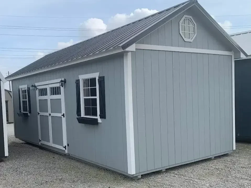 a large garden shed with double doors with transom windows in them. It also has two windows with shutters