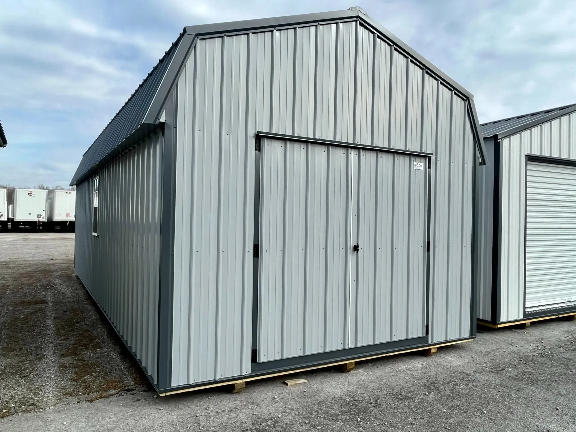 a large gray metal lofted barn with double doors in the front and a window on the left wall