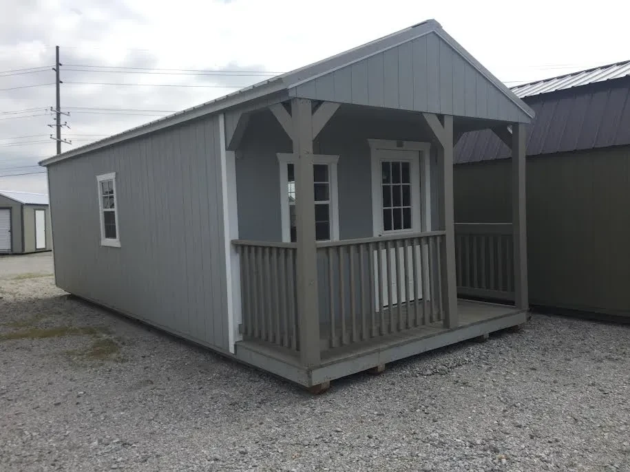a gray cabin with a porch and a walk-in door and multiple windows