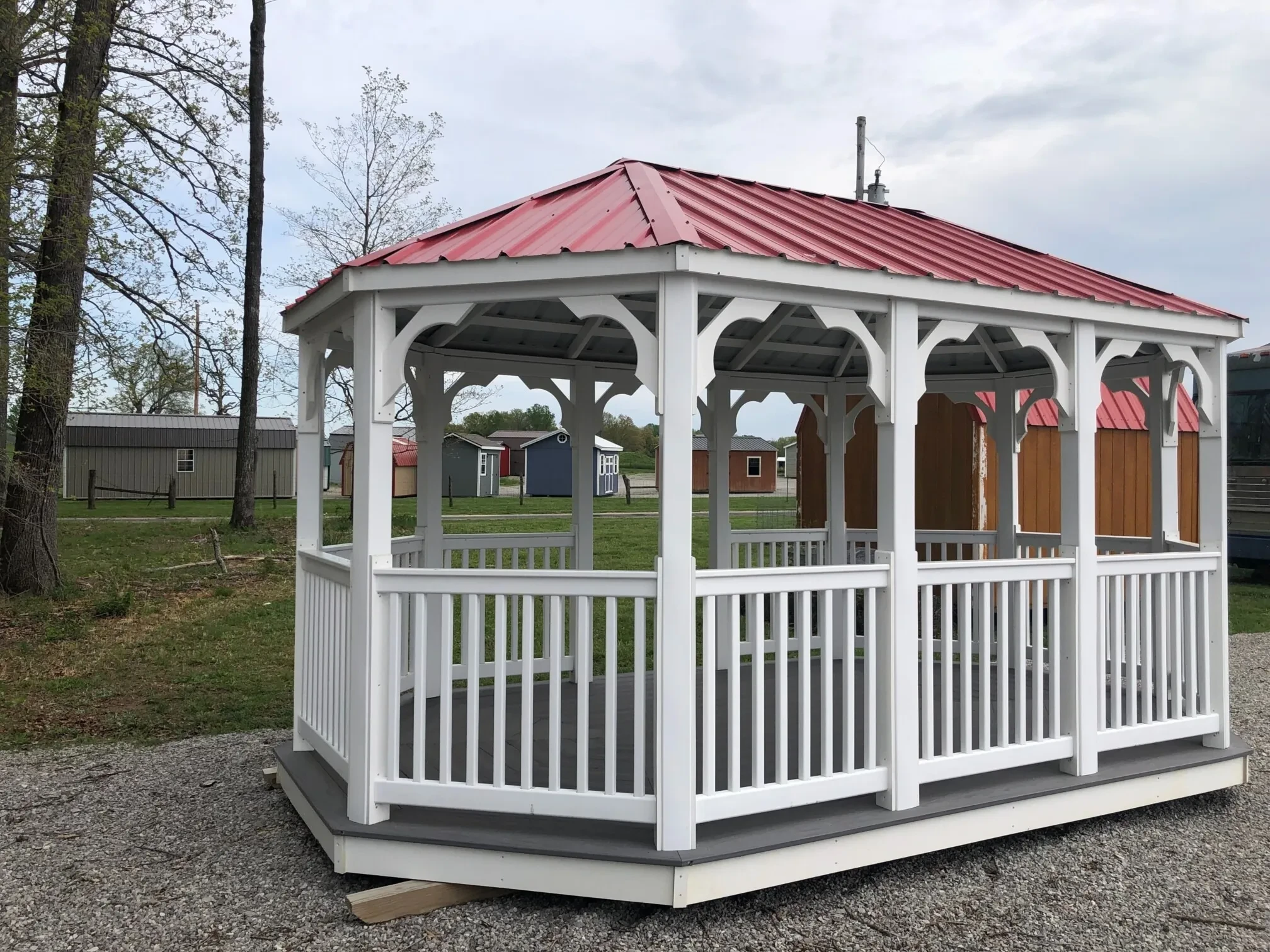 a large white vinyl gazebo with posts and railings. It also has a red metal roof