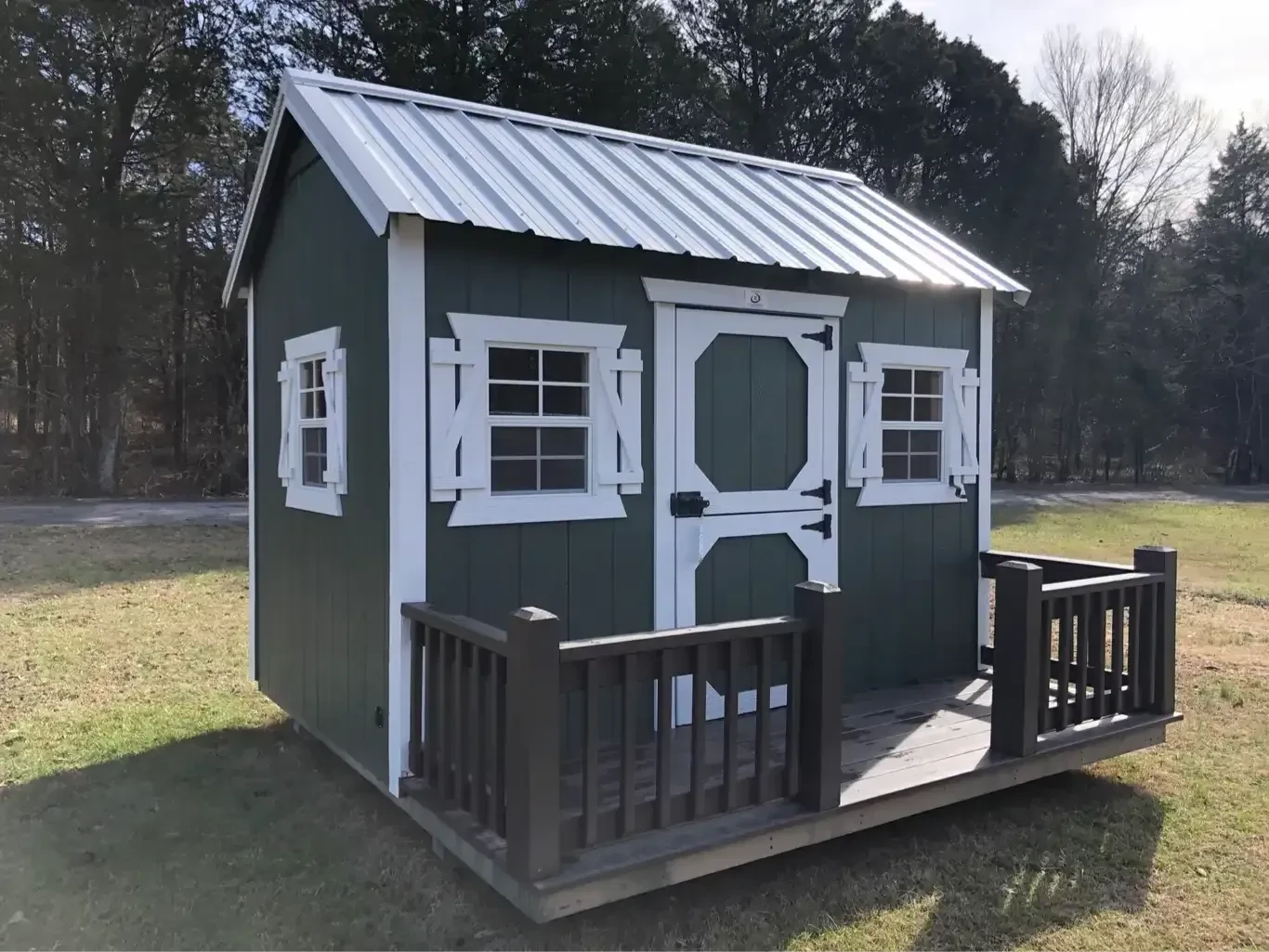 a green playhouse with white trim and a brown porch. it has a white metal roof