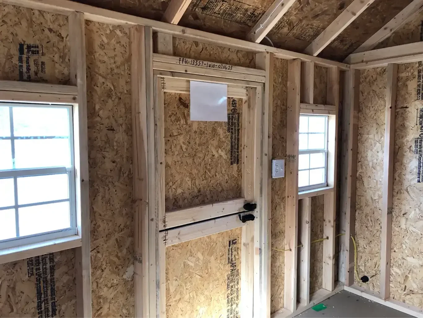 inside a wood playhouse looking at the back of the door which is a single door in half and it has two small windows