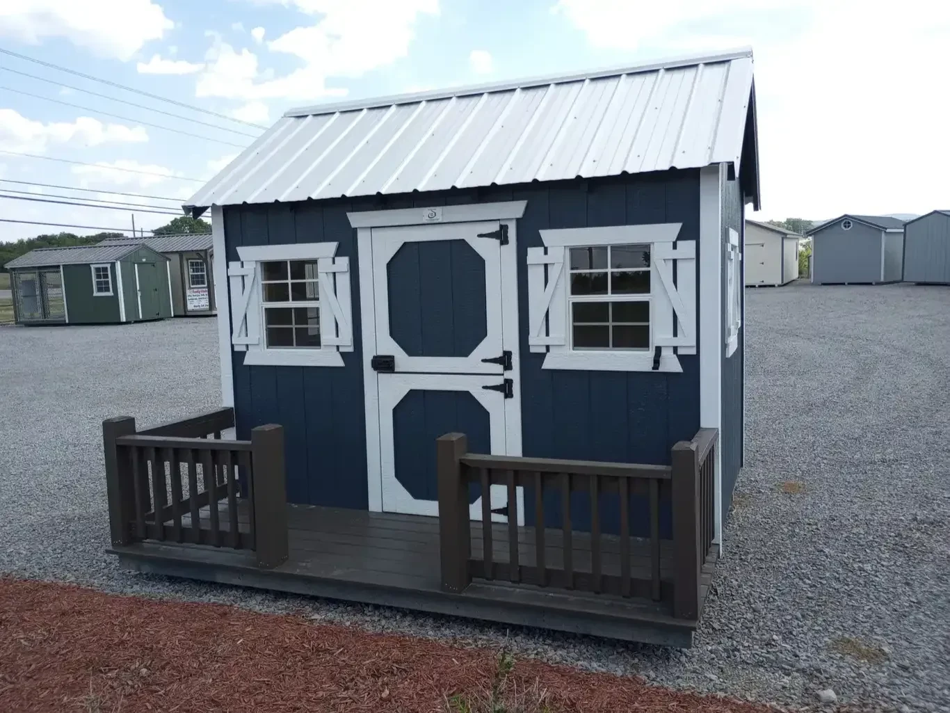 a wood playhouse painted blue with white trim and a porch with posts and railings. it has windows with shutters