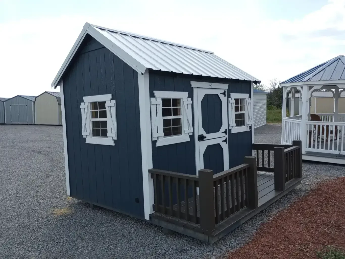 the front corner view of a blue playhouse with white trim and a white metal roof