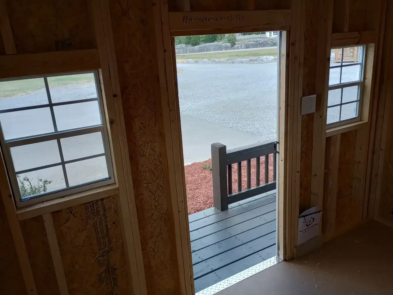 inside a wood playhouse looking through the wood door which is open towards the little porch