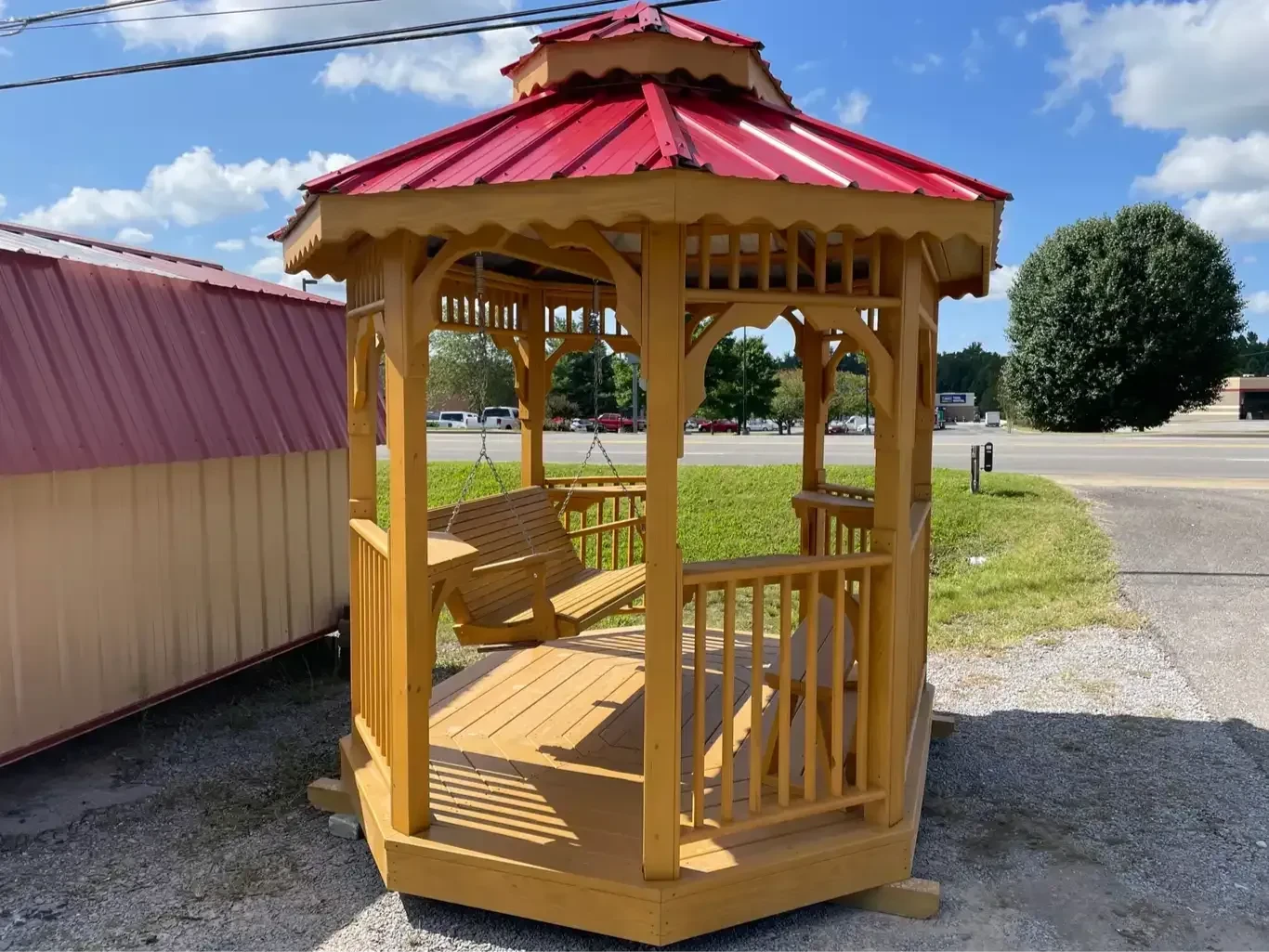 a wood teahouse that is a stained wood color with a red metal roof and swinging chairs inside